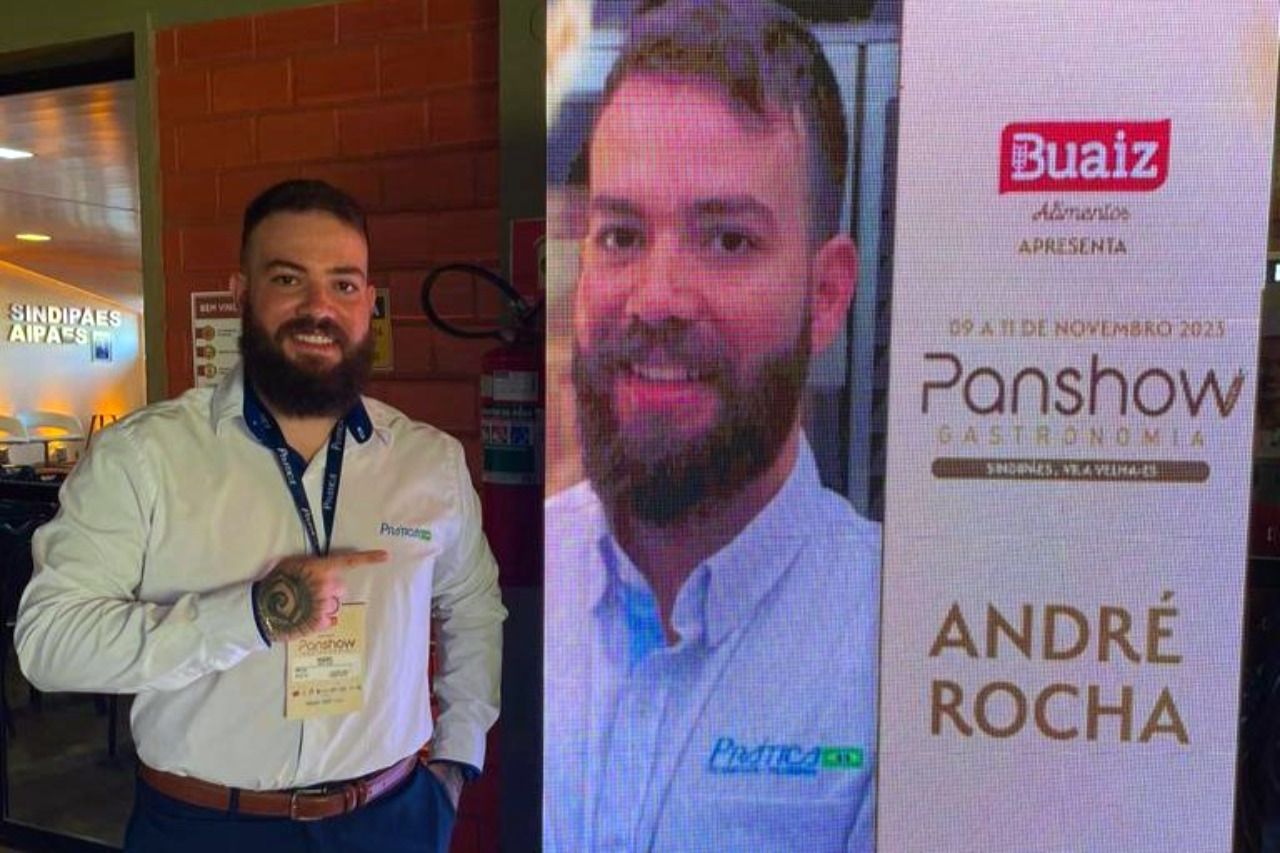 Um homem com barba está parado em frente a uma placa que diz andre rocha.