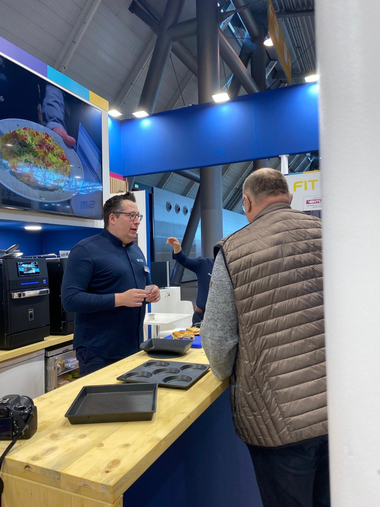 Dois homens estão em pé no balcão de uma cozinha conversando um com o outro.