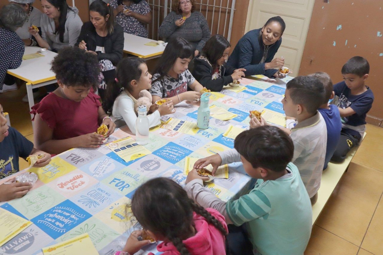 Um grupo de crianças está sentado à mesa comendo sanduíches.