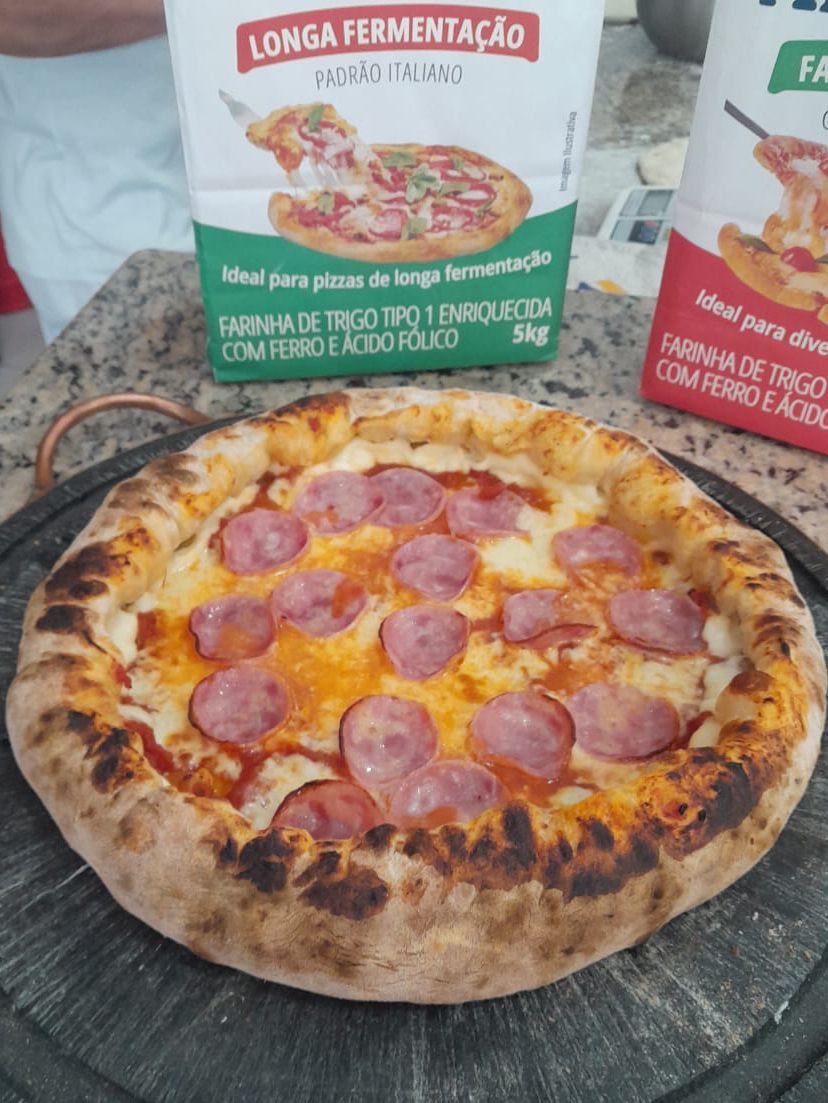 Uma pizza está sobre uma mesa ao lado de uma caixa de longa fermentação