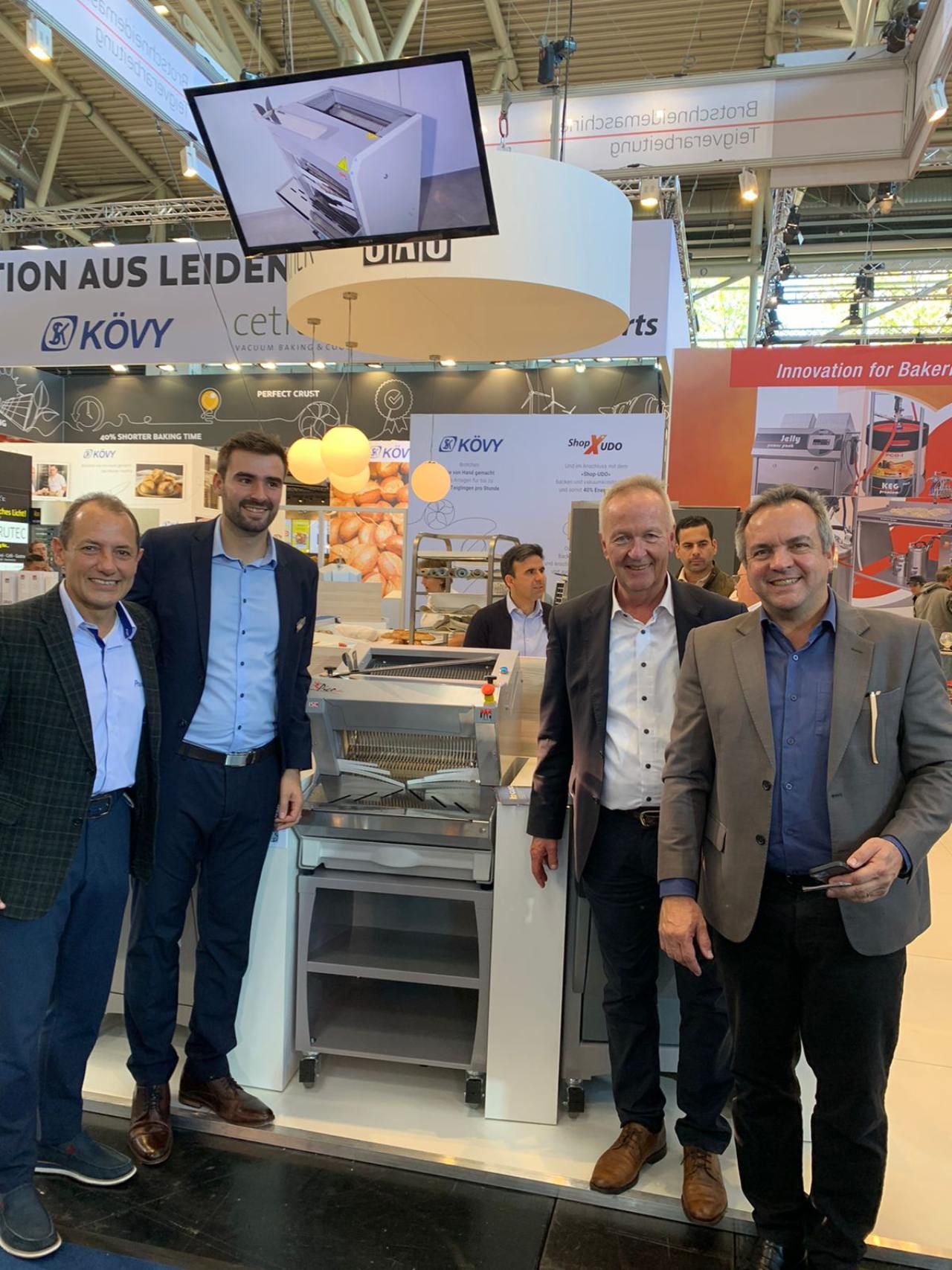 Um grupo de homens está posando para uma foto em frente a um estande em uma convenção.