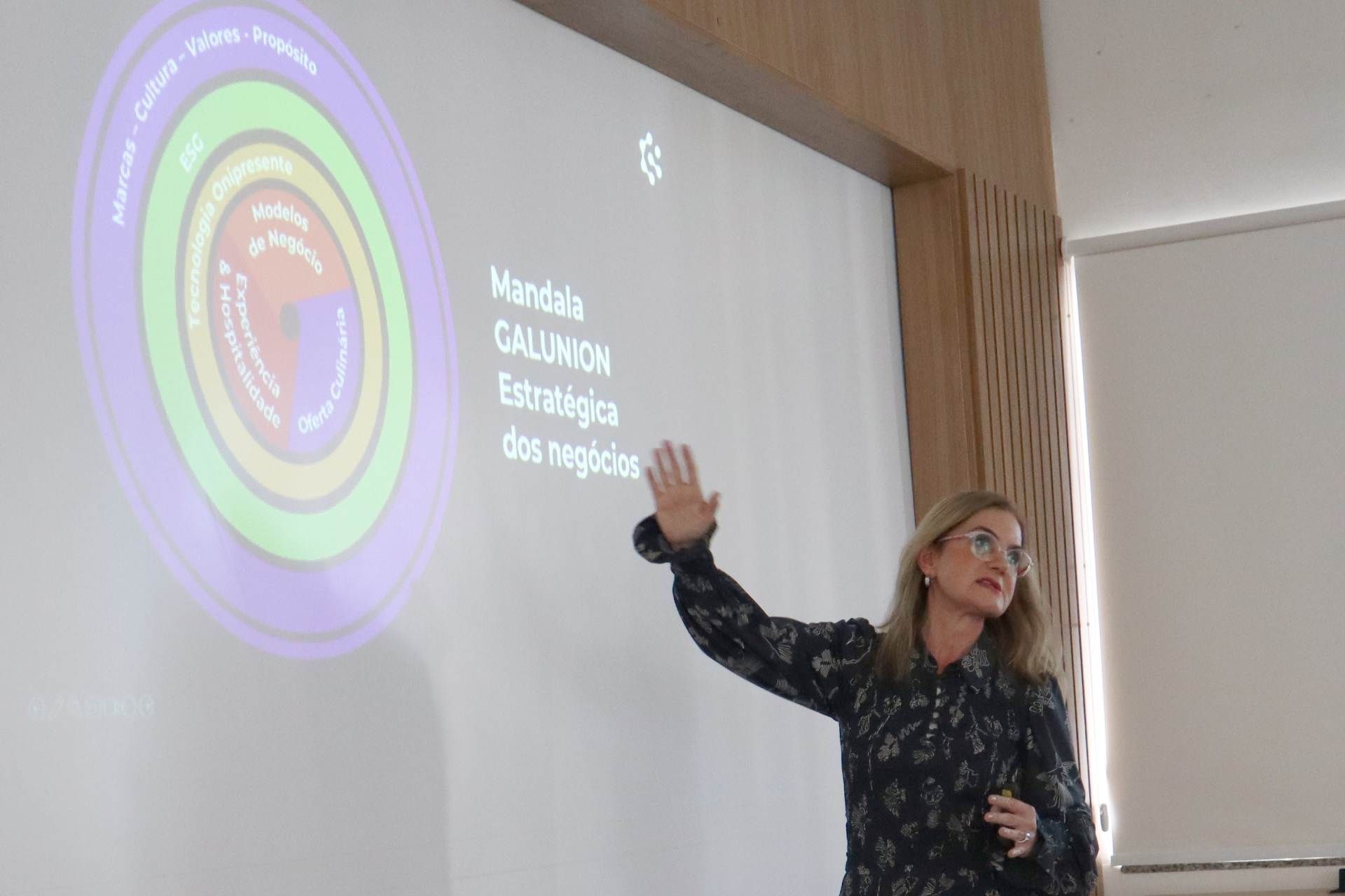Uma mulher está fazendo uma apresentação em frente a uma tela grande.