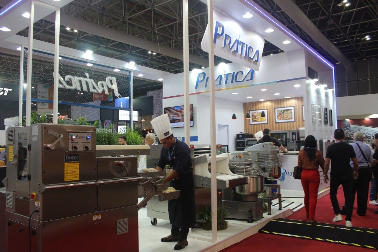 Um homem com chapéu de chef está diante de um estande em uma convenção.