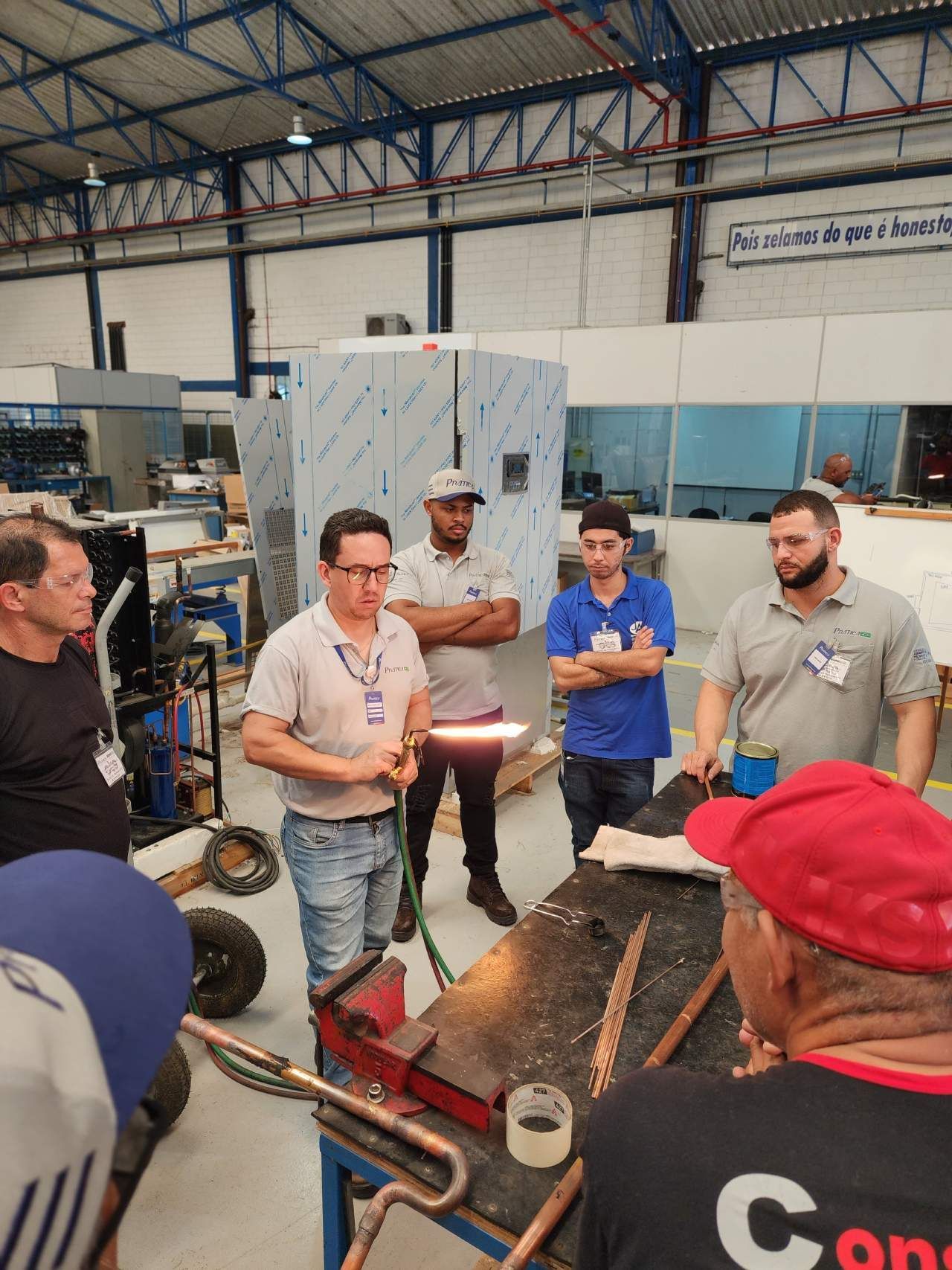 Um grupo de homens está em volta de uma mesa em uma fábrica.