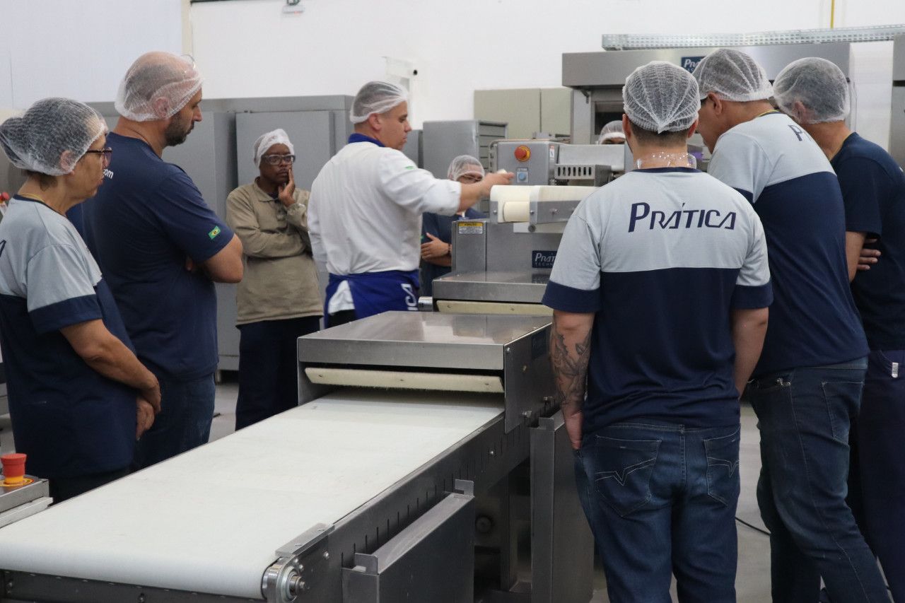 Um grupo de pessoas está em pé ao redor de uma esteira rolante em uma cozinha.