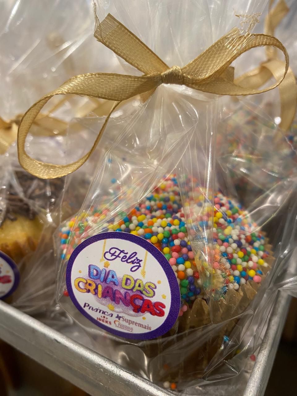 A bag of cupcakes with sprinkles and a sticker that says feliz dia das crianças