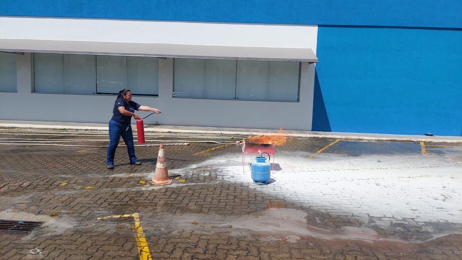 Uma mulher está usando um extintor de incêndio para apagar um incêndio em um estacionamento.