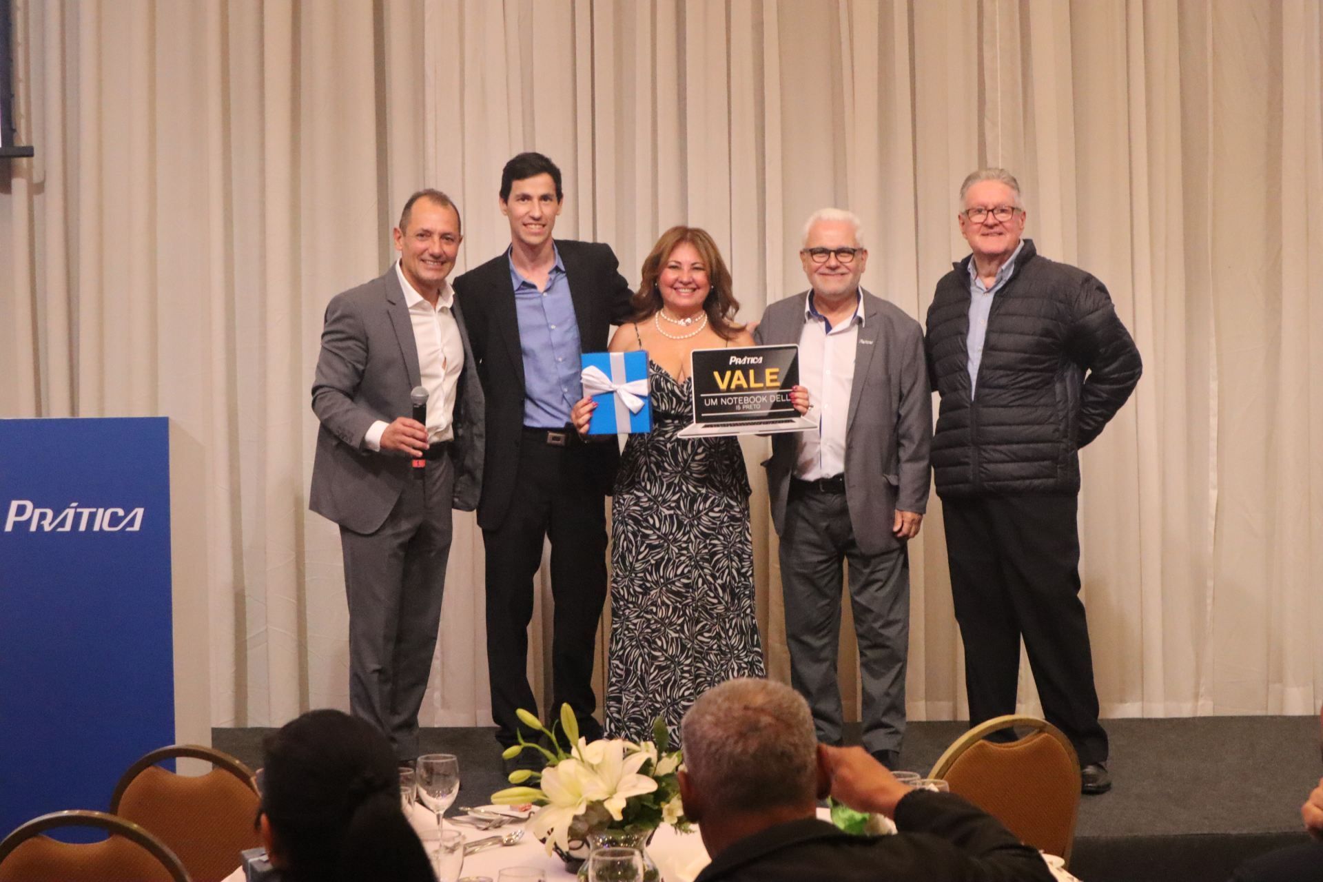 Um grupo de pessoas está posando para uma foto com uma mulher segurando uma caixa de presente.