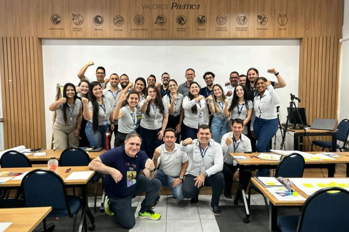 Grupo de pessoas sorridentes posando juntas em uma sala de aula, algumas flexionando os braços, demonstrando entusiasmo.