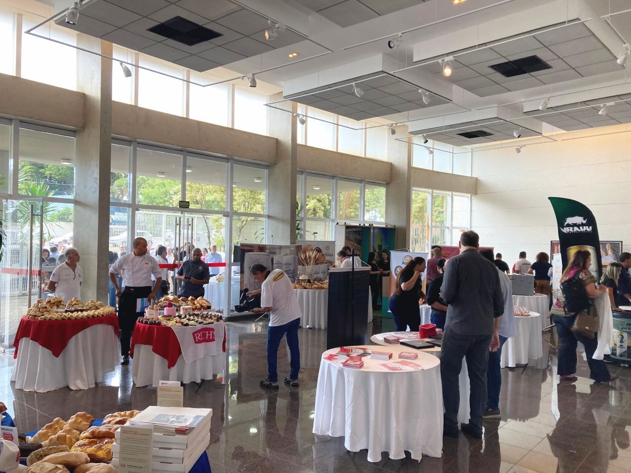 Um grupo de pessoas está em volta de mesas em uma grande sala.