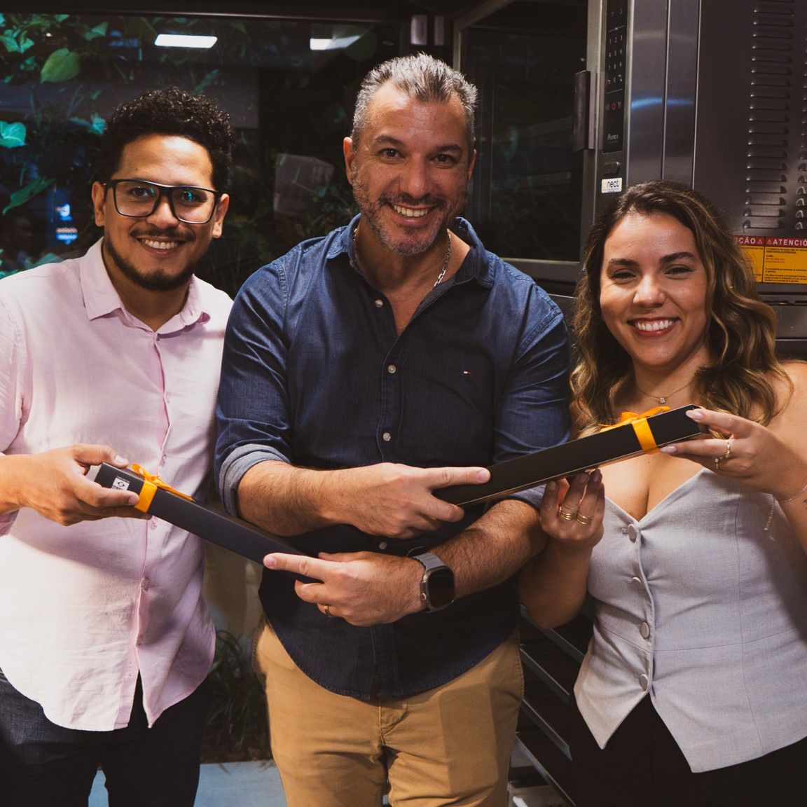 Três pessoas estão posando para uma foto e uma delas está segurando um objeto grande