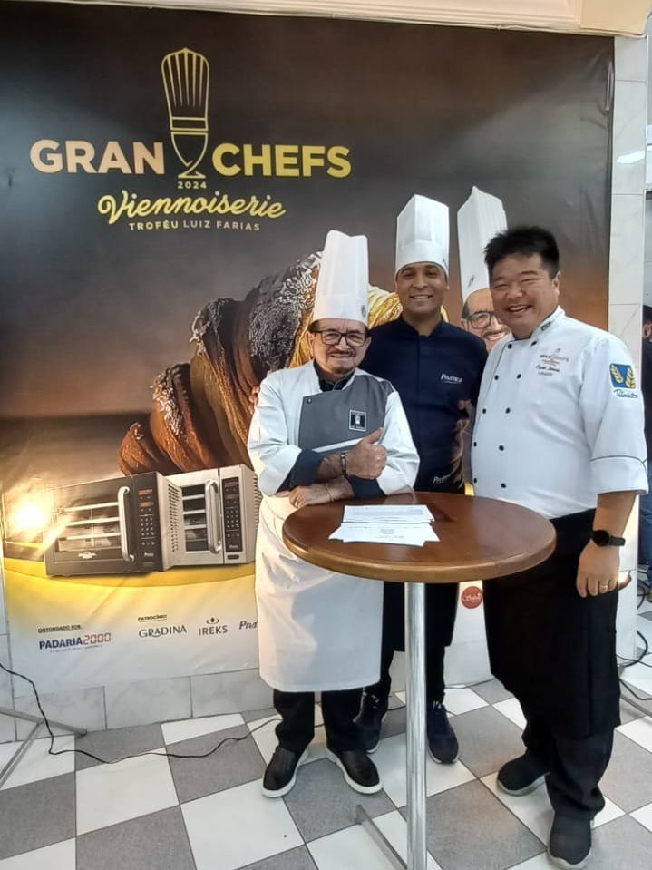 Três chefs estão de pé, um ao lado do outro, em frente a uma placa que diz gran chefs.