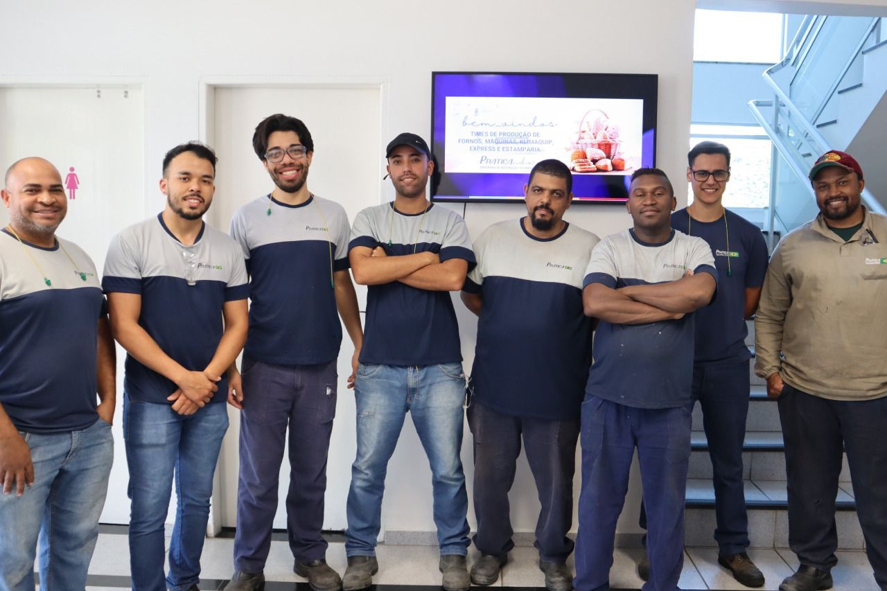 Um grupo de homens está posando para uma foto em frente a uma televisão.