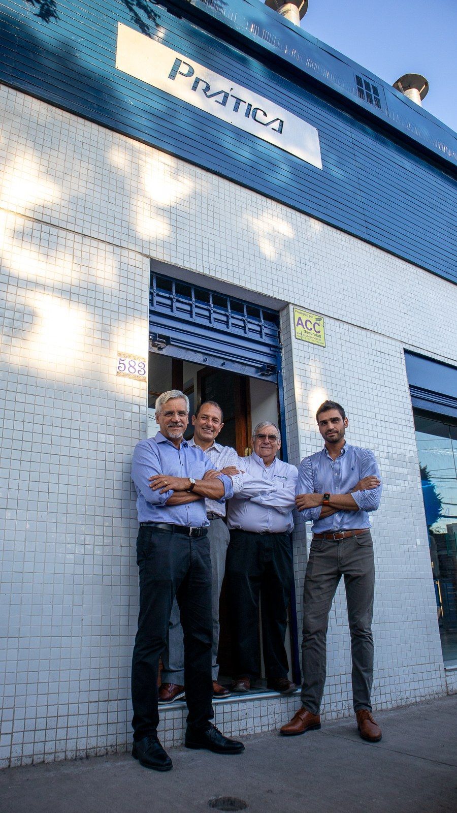 Um grupo de homens está parado em frente a um prédio com os braços cruzados.