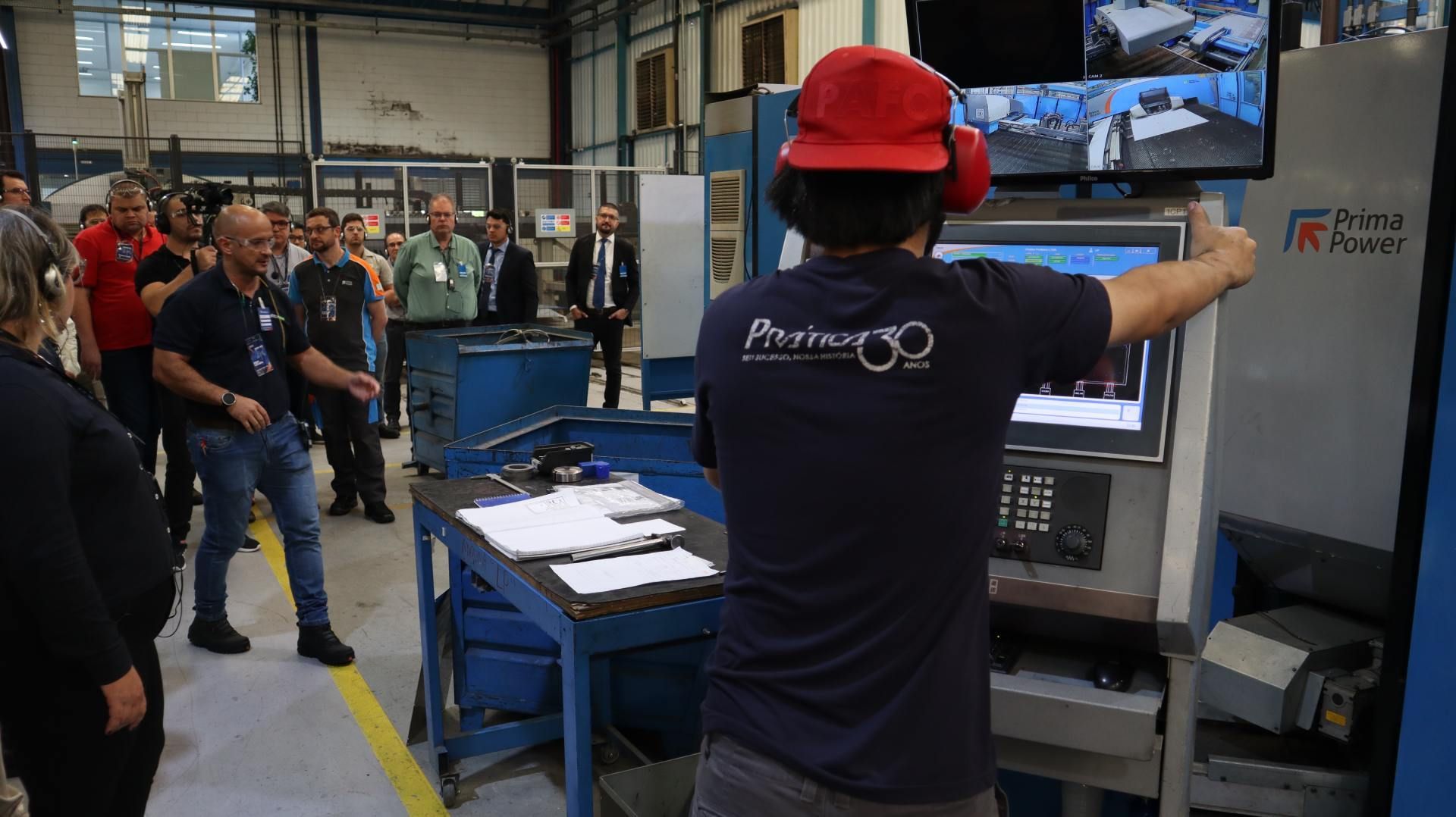 Um homem usando um capacete vermelho está parado em frente a um computador em uma fábrica.