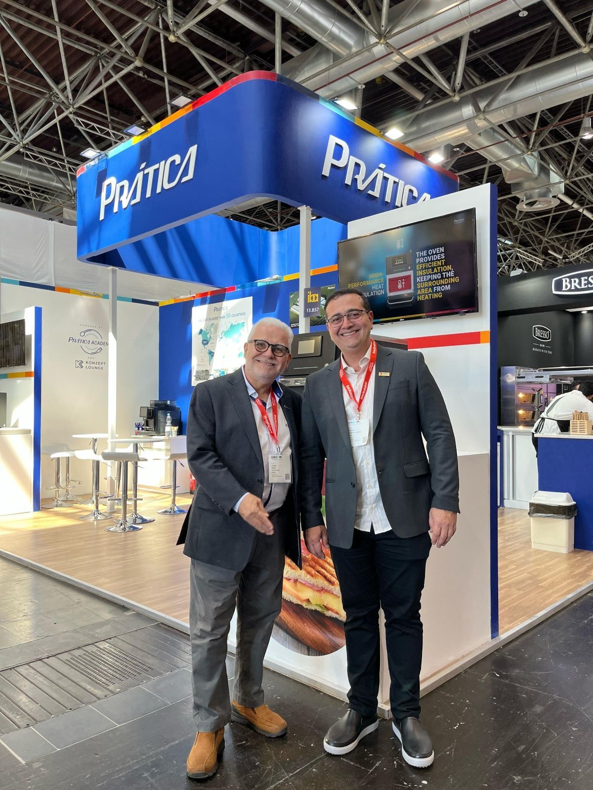 Dois homens estão parados um ao lado do outro em frente a um estande em uma convenção.