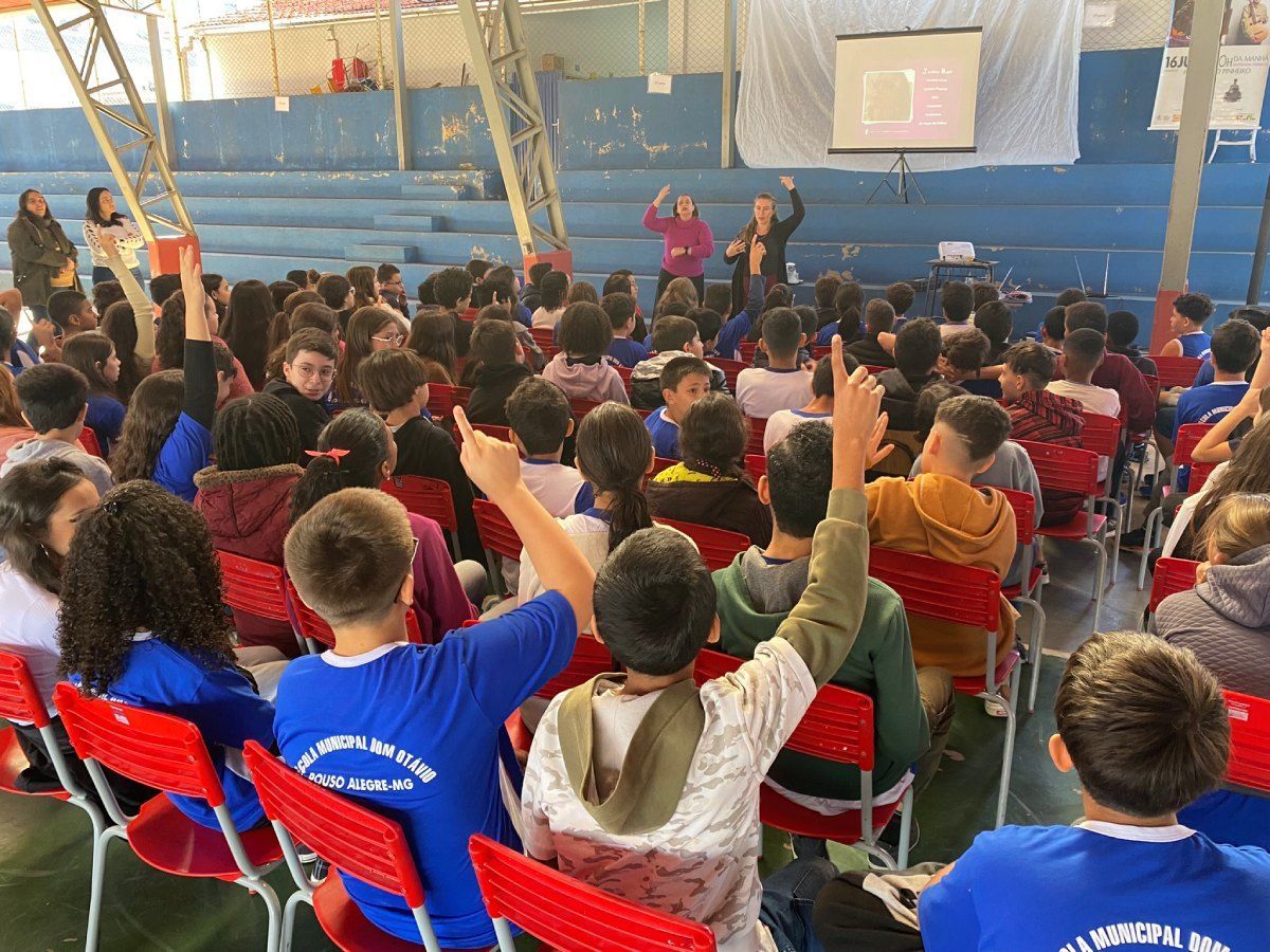 Um grupo de crianças está sentado em um estádio levantando as mãos para responder a uma pergunta.