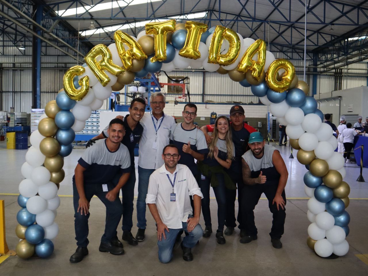 Um grupo de pessoas está posando para uma foto sob um arco de balões que diz gratidao