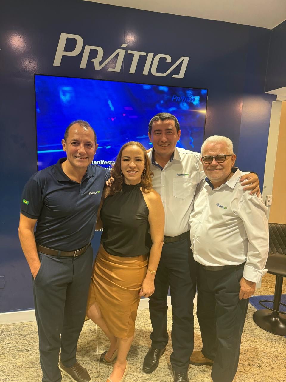 Quatro pessoas sorrindo, posadas em frente a uma parede azul com a palavra 