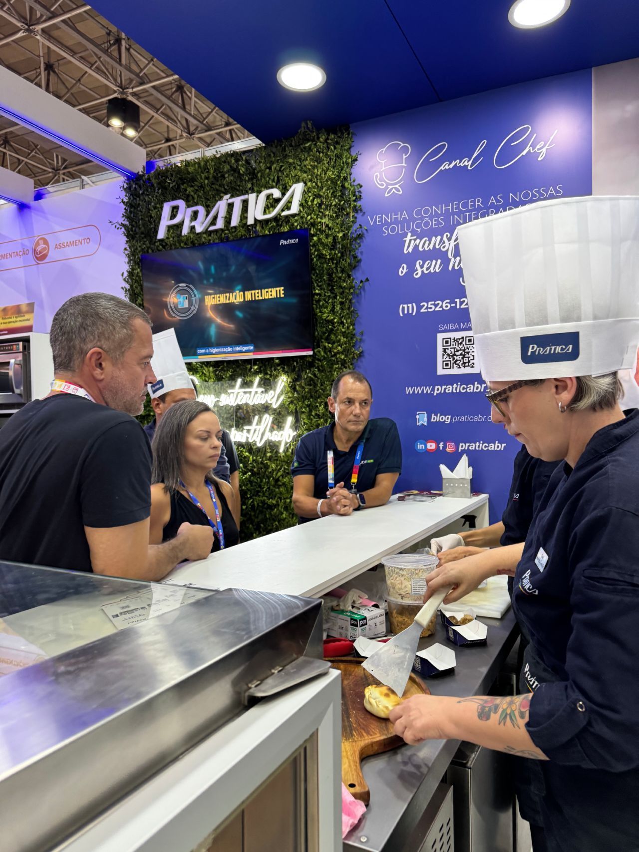 Um grupo de pessoas está em pé ao redor de um balcão em uma cozinha.