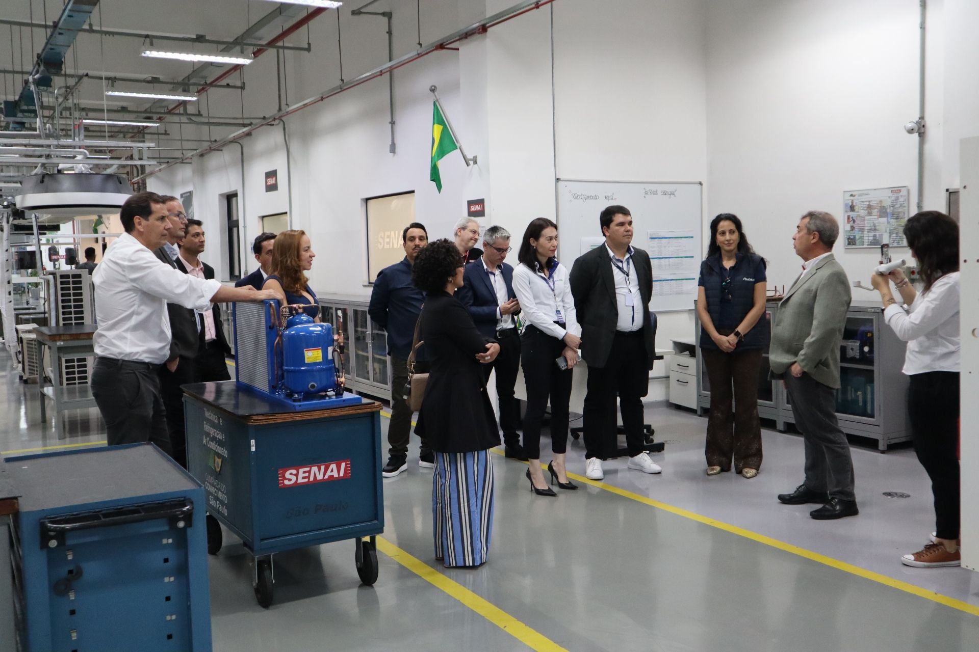 Grupo de pessoas visitando uma fábrica. Elas estão observando uma unidade de refrigeração.