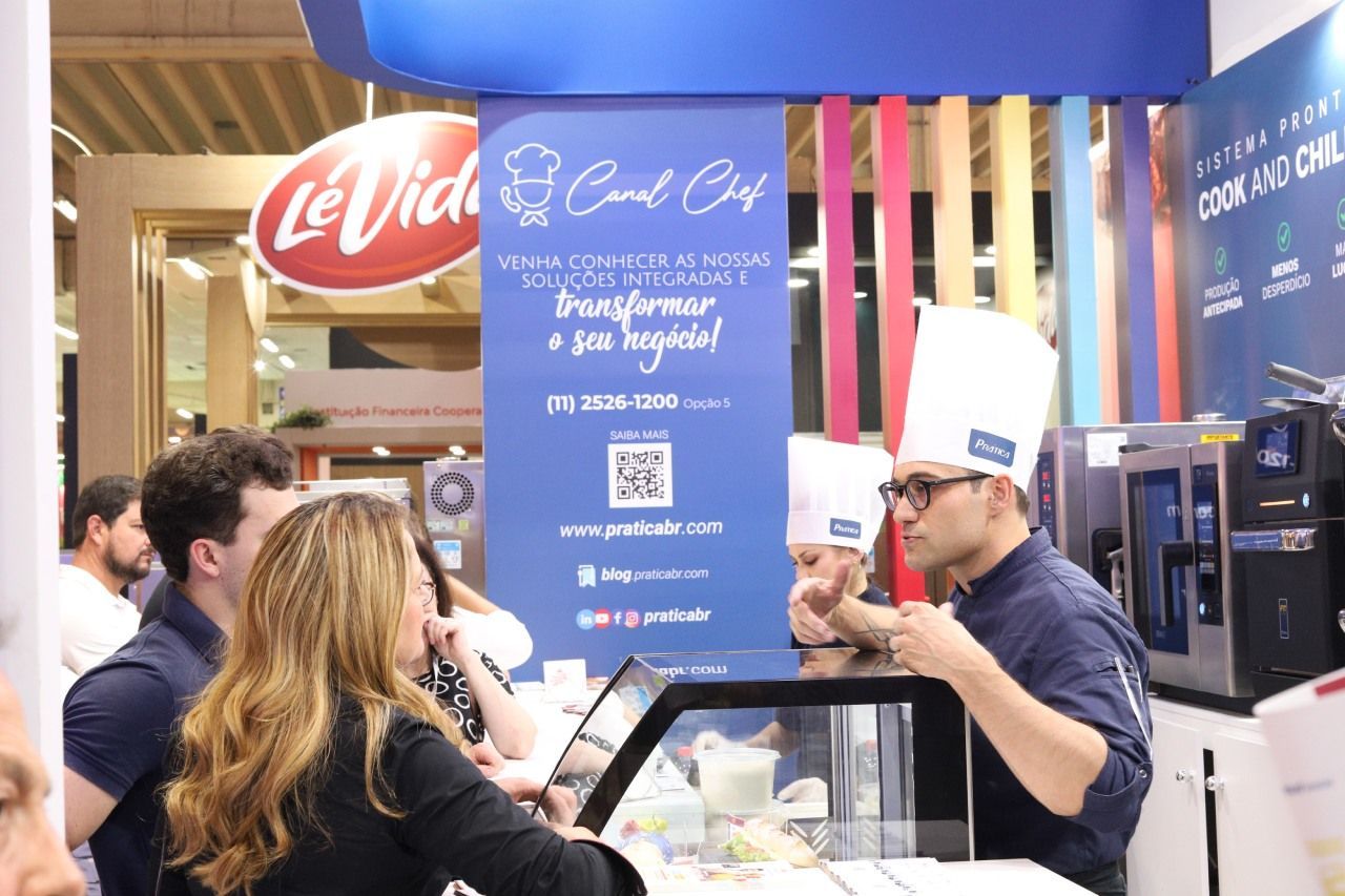 Um homem com chapéu de chef está conversando com uma mulher em frente a uma placa que diz le vida