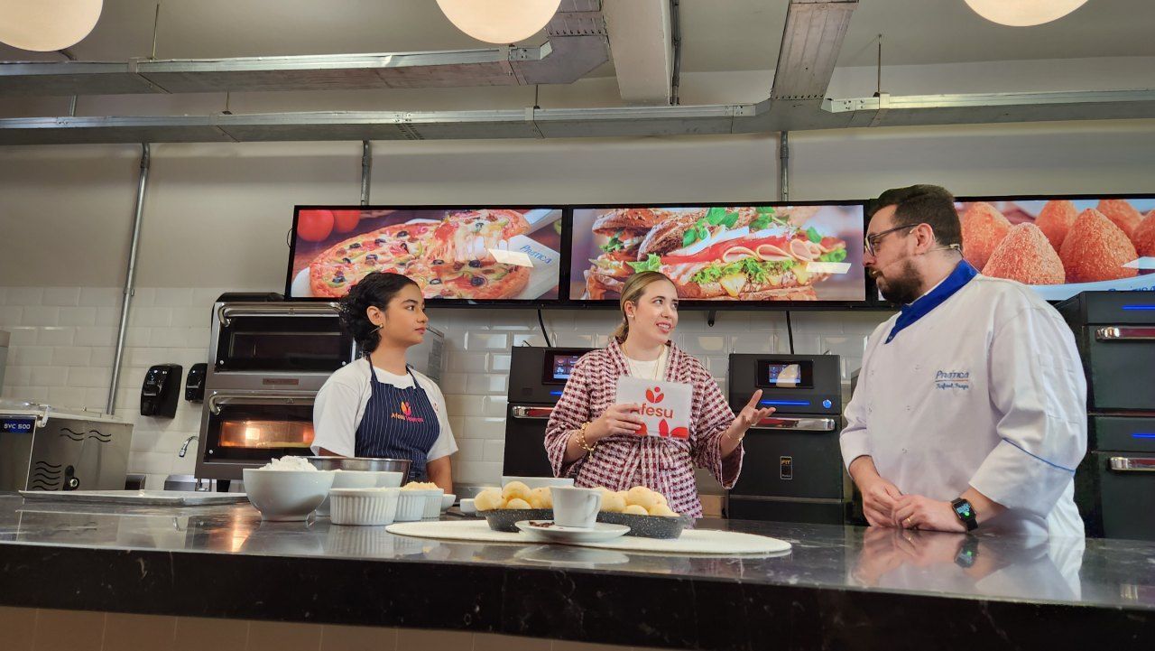 Um homem e duas mulheres estão em uma cozinha conversando um com o outro.