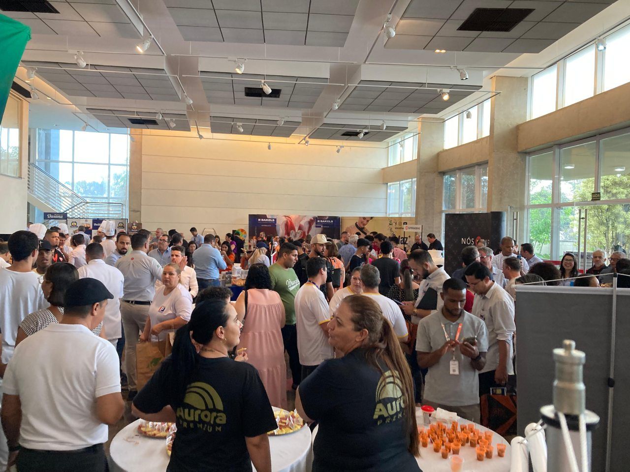 Um grande grupo de pessoas está em volta de mesas em uma grande sala.