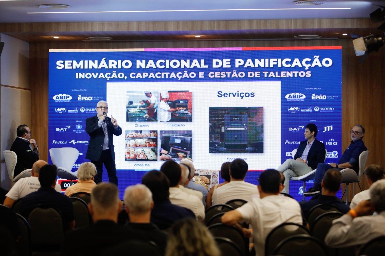 Um grupo de pessoas está sentado em frente a uma tela que diz seminário nacional de panificação