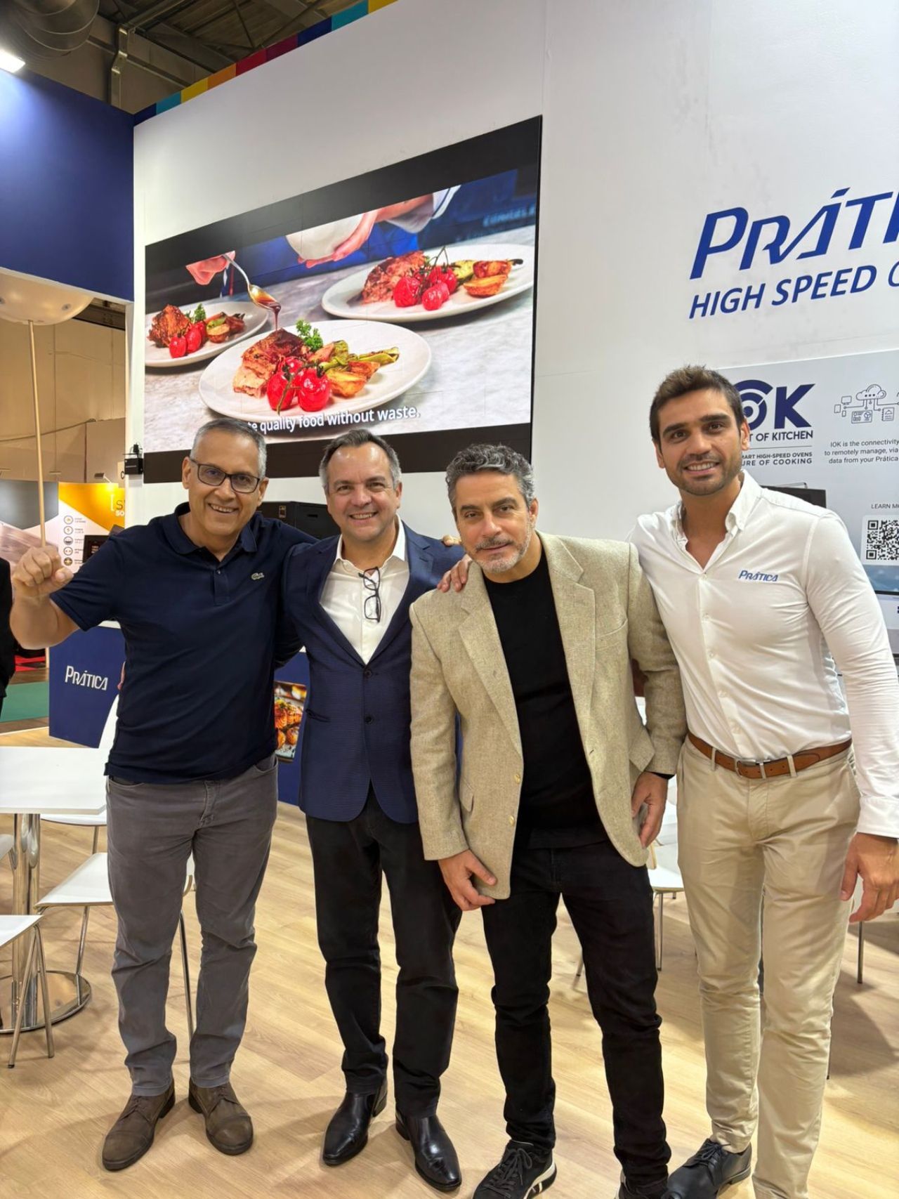 Quatro homens posam em frente a um estande com uma exposição de alimentos e o logotipo da empresa.