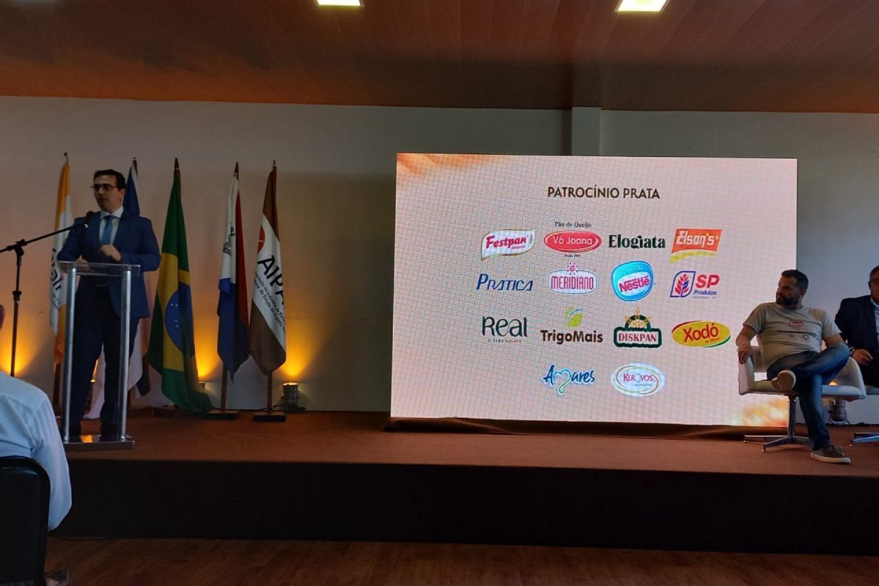 Um homem está em um pódio fazendo uma apresentação em frente a uma tela grande.