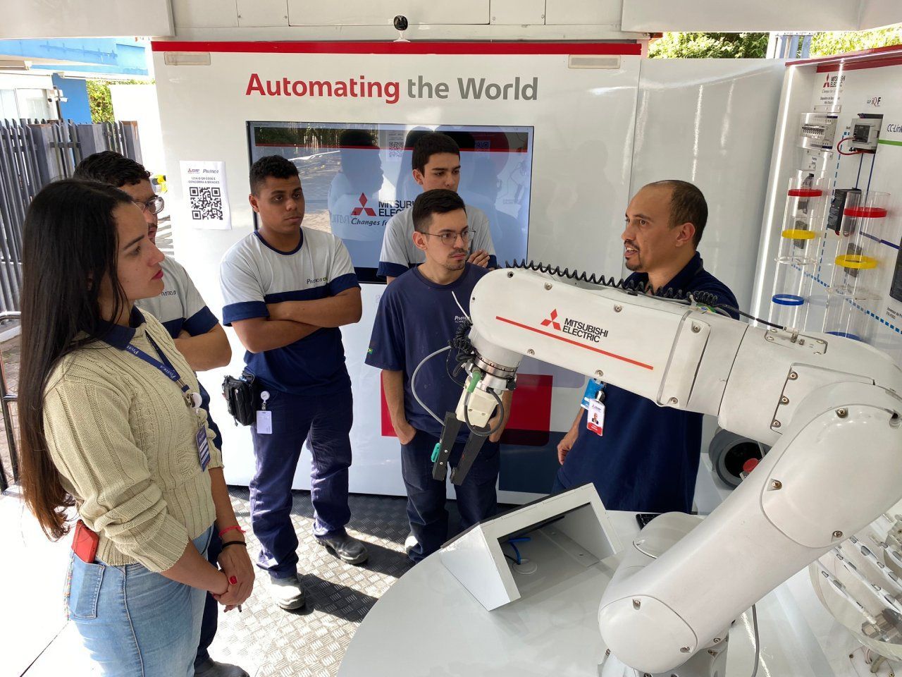 Um grupo de pessoas está em pé ao redor de um braço robótico.