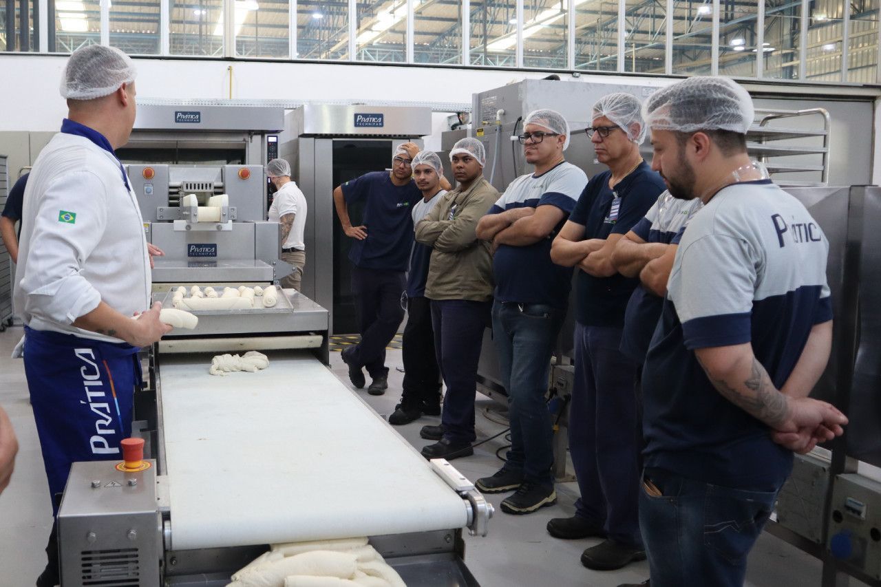 Um grupo de homens está em pé ao redor de uma correia transportadora em uma fábrica.