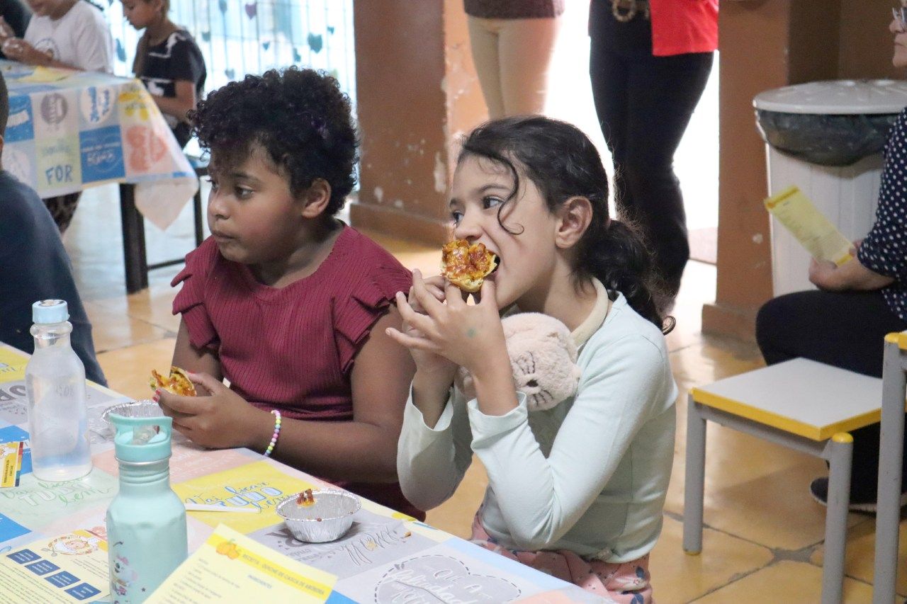 Duas jovens estão sentadas à mesa comendo pizza.