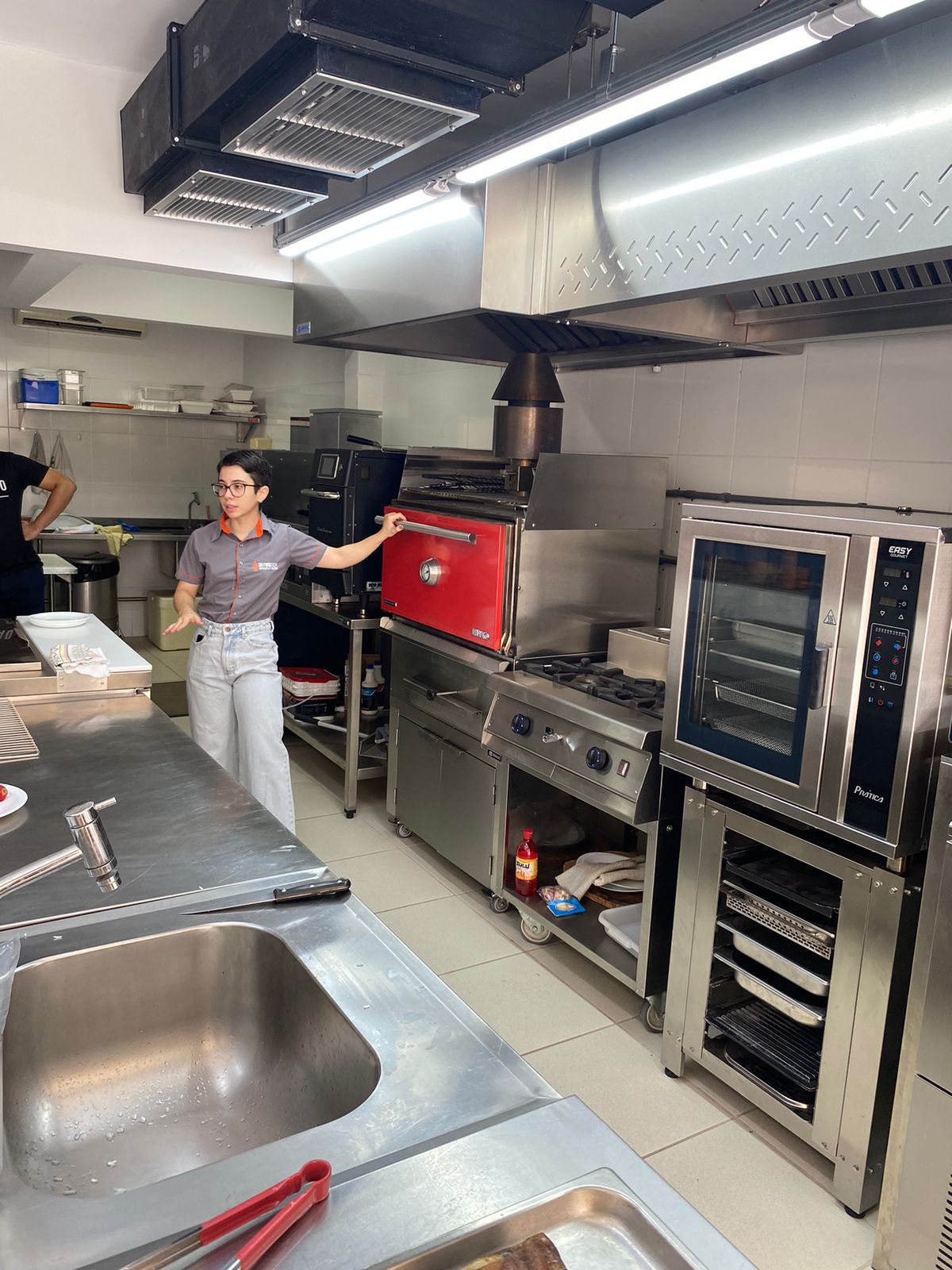 Uma mulher está parada na cozinha segurando um forno vermelho.