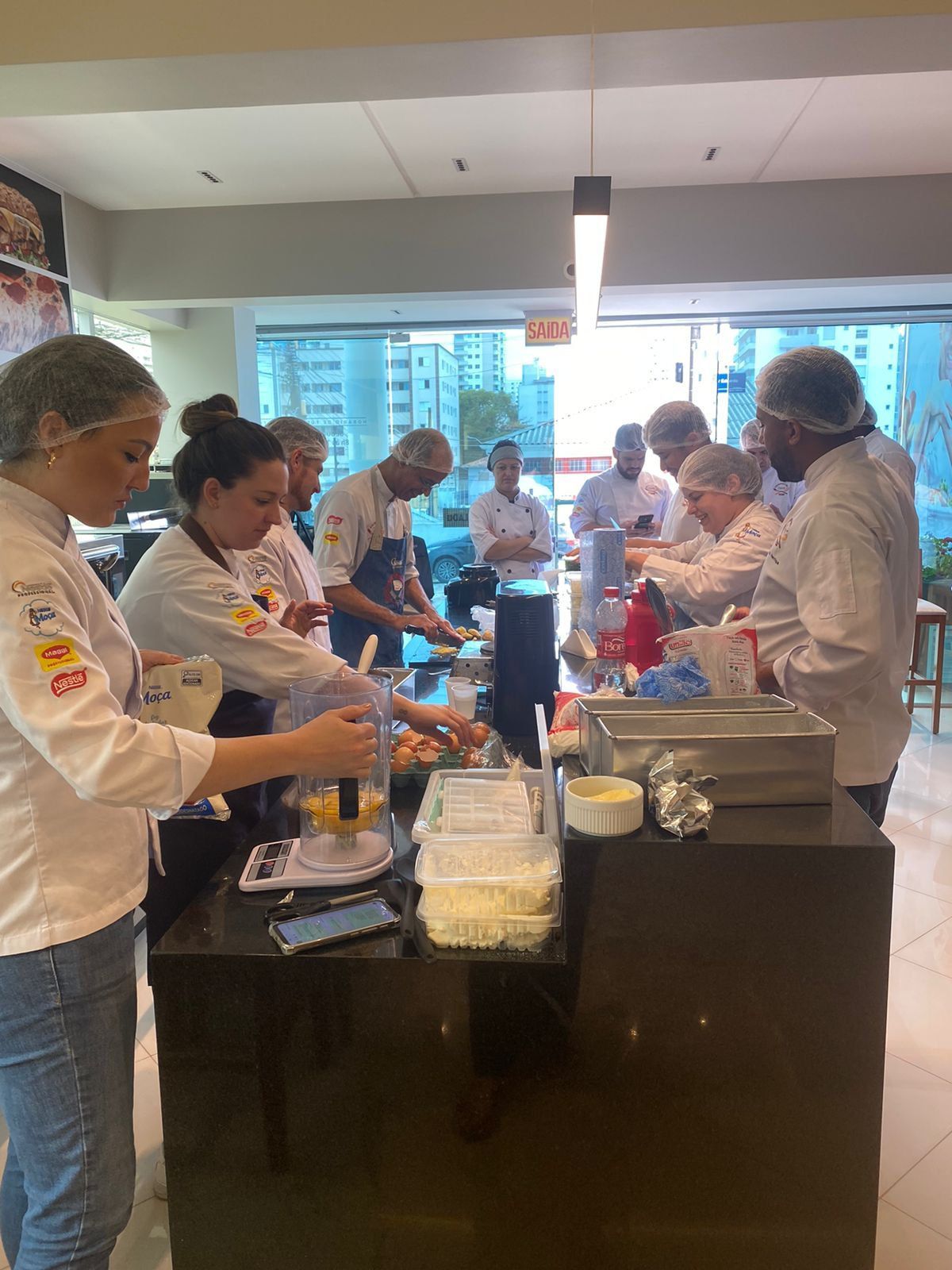Um grupo de pessoas está em pé ao redor de uma mesa na cozinha preparando comida.