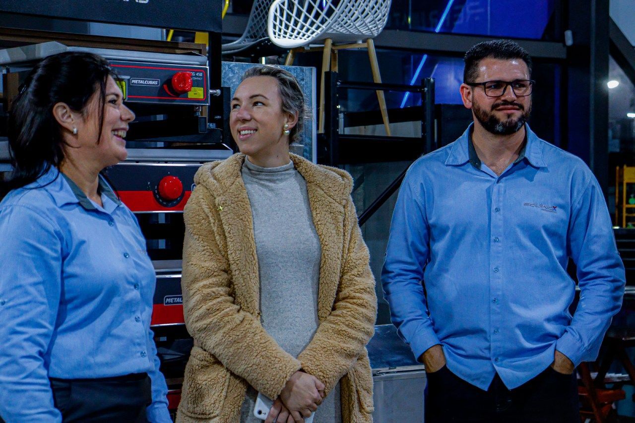 Um homem e duas mulheres estão de pé, um ao lado do outro, em uma sala.