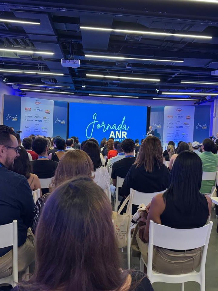 Um grupo de pessoas está sentado em cadeiras em frente a uma tela grande.