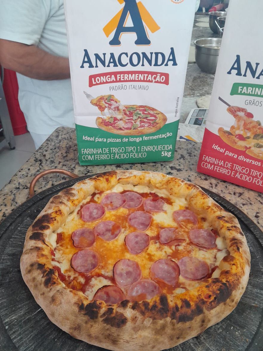 Uma pizza está sobre uma mesa ao lado de uma caixa de farinha de anaconda.