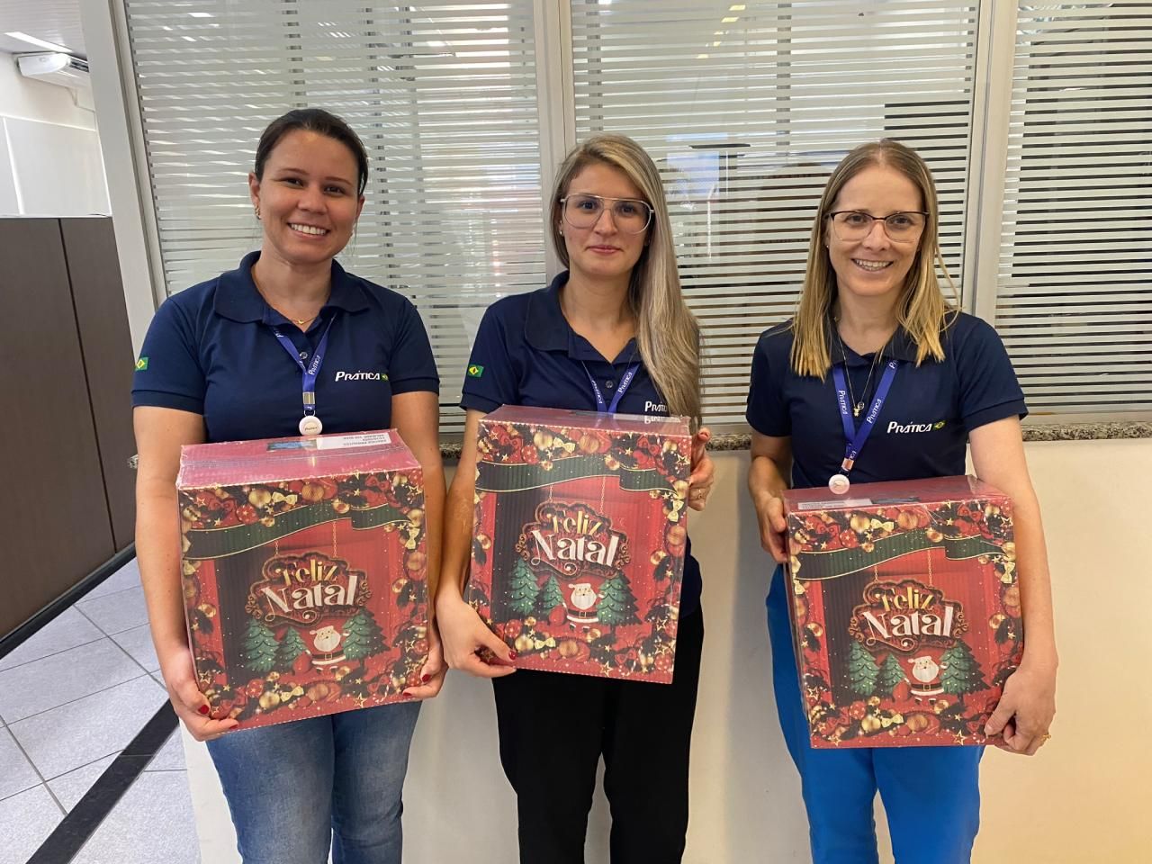 Três mulheres estão segurando caixas de natal em frente a uma janela.