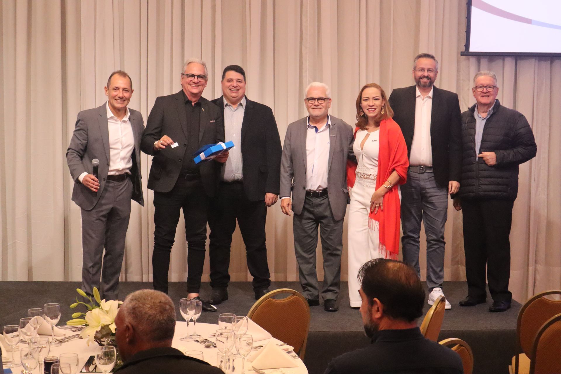 Um grupo de homens e mulheres estão posando para uma foto em uma conferência.