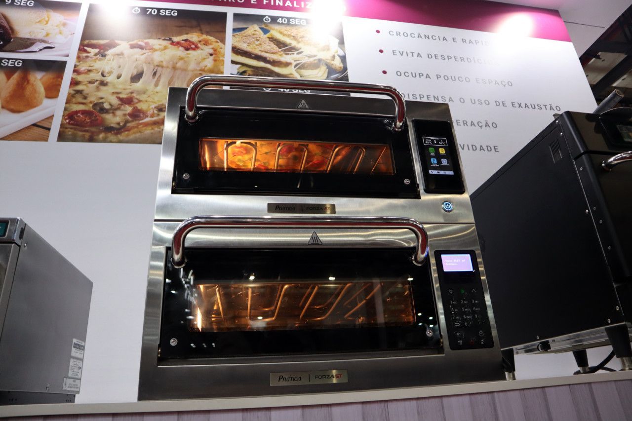 Um forno de aço inoxidável com uma exposição de pizzas na parede atrás dele