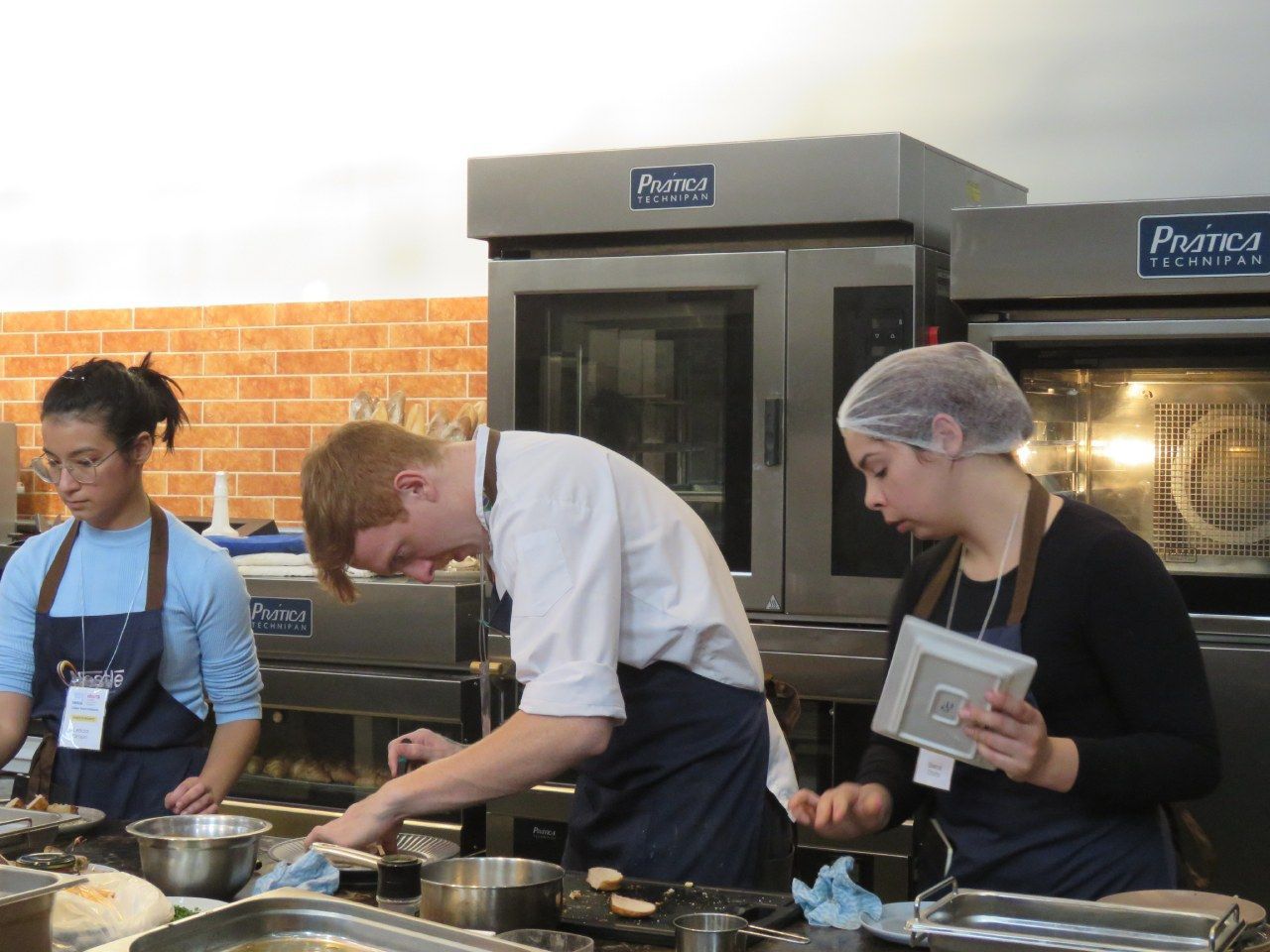 Um homem e duas mulheres estão preparando comida em uma cozinha com um forno que diz prima