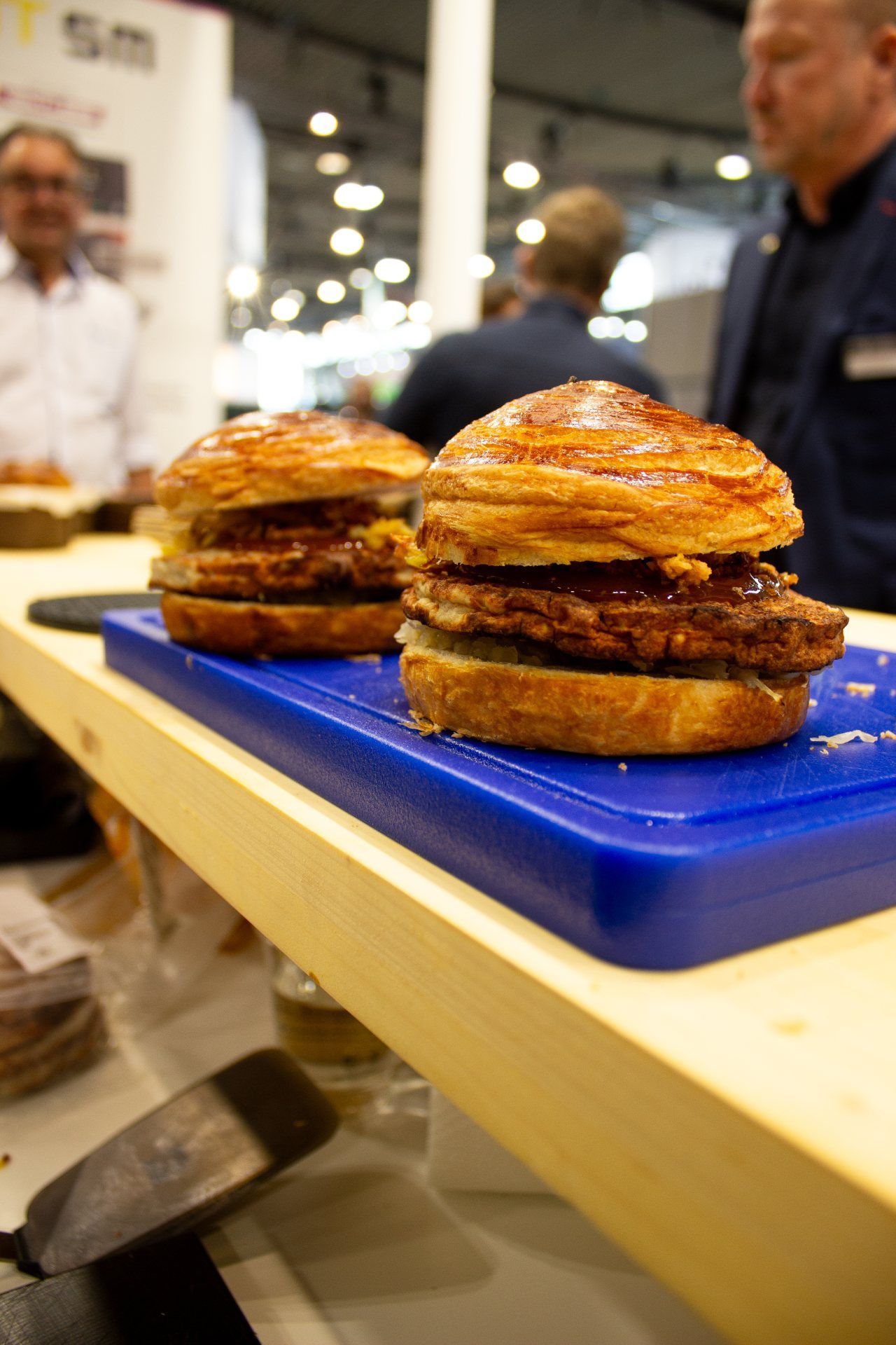 Dois hambúrgueres estão sobre uma tábua de corte azul sobre uma mesa.