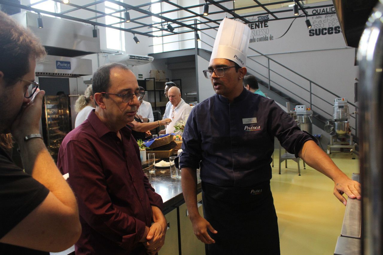 Um homem com chapéu de chef está conversando com outro homem na cozinha.