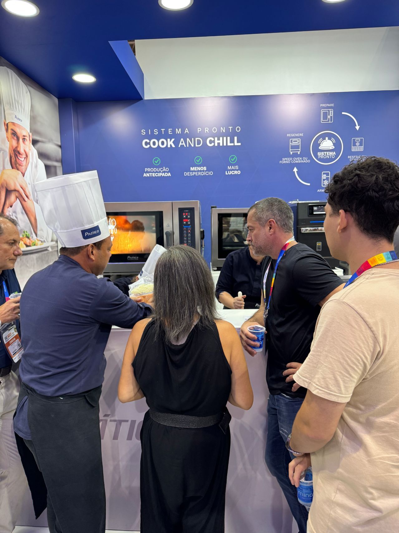 Um grupo de pessoas está em pé ao redor de um balcão em uma sala.