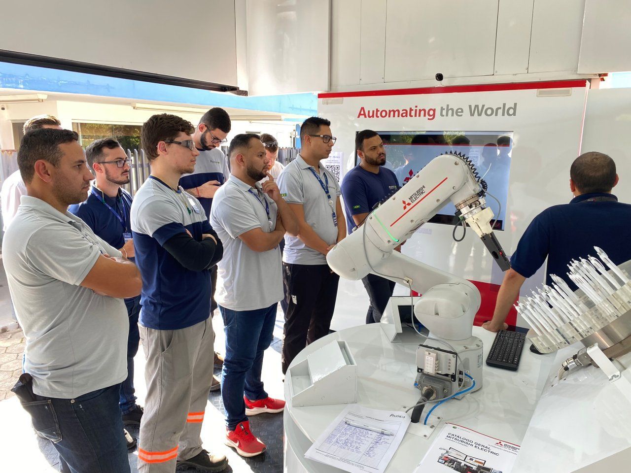 Um grupo de homens está em pé ao redor de um braço robótico em uma sala.