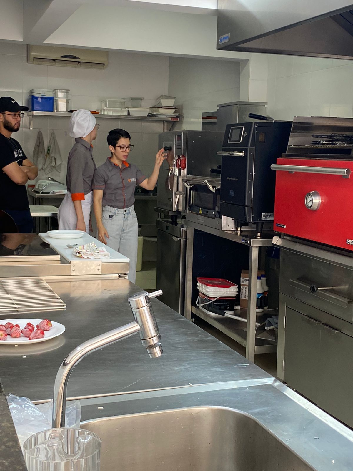 Um grupo de pessoas está trabalhando em uma cozinha com uma pia e um forno vermelho.