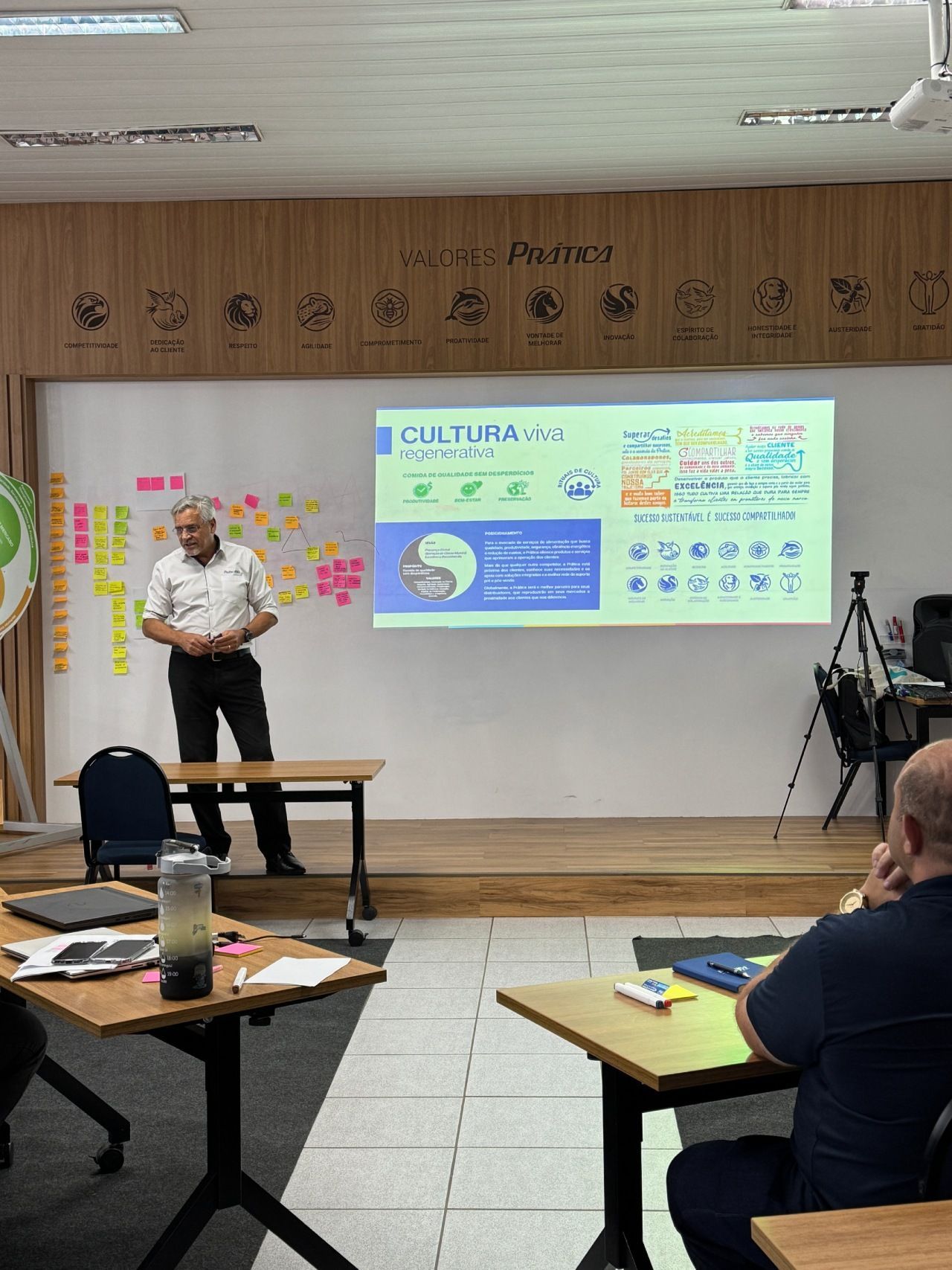 Um apresentador está em pé ao lado de uma tela que exibe “LOGÍSTICA VERDE”