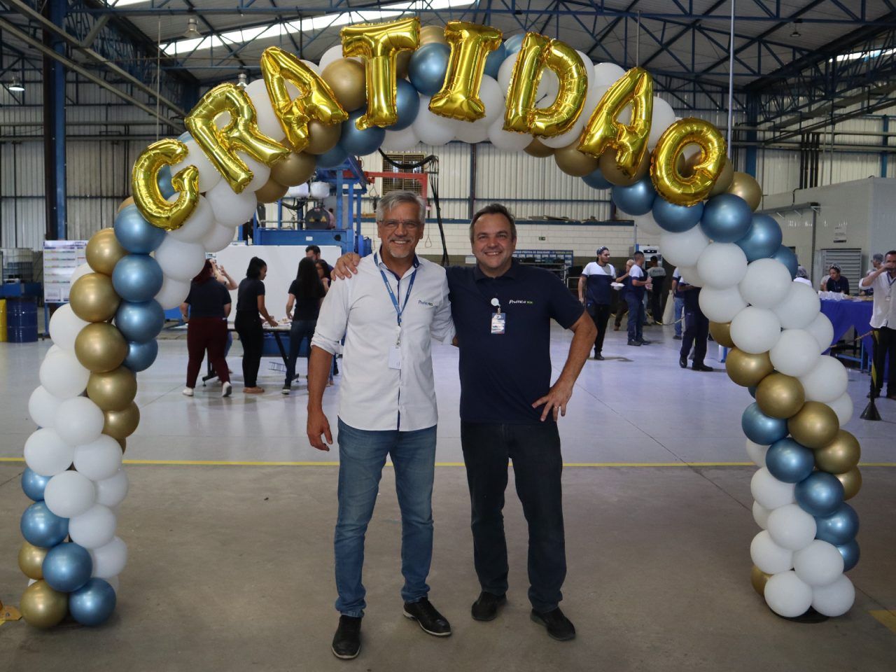 Dois homens estão parados sob um arco de balões que diz gratidao